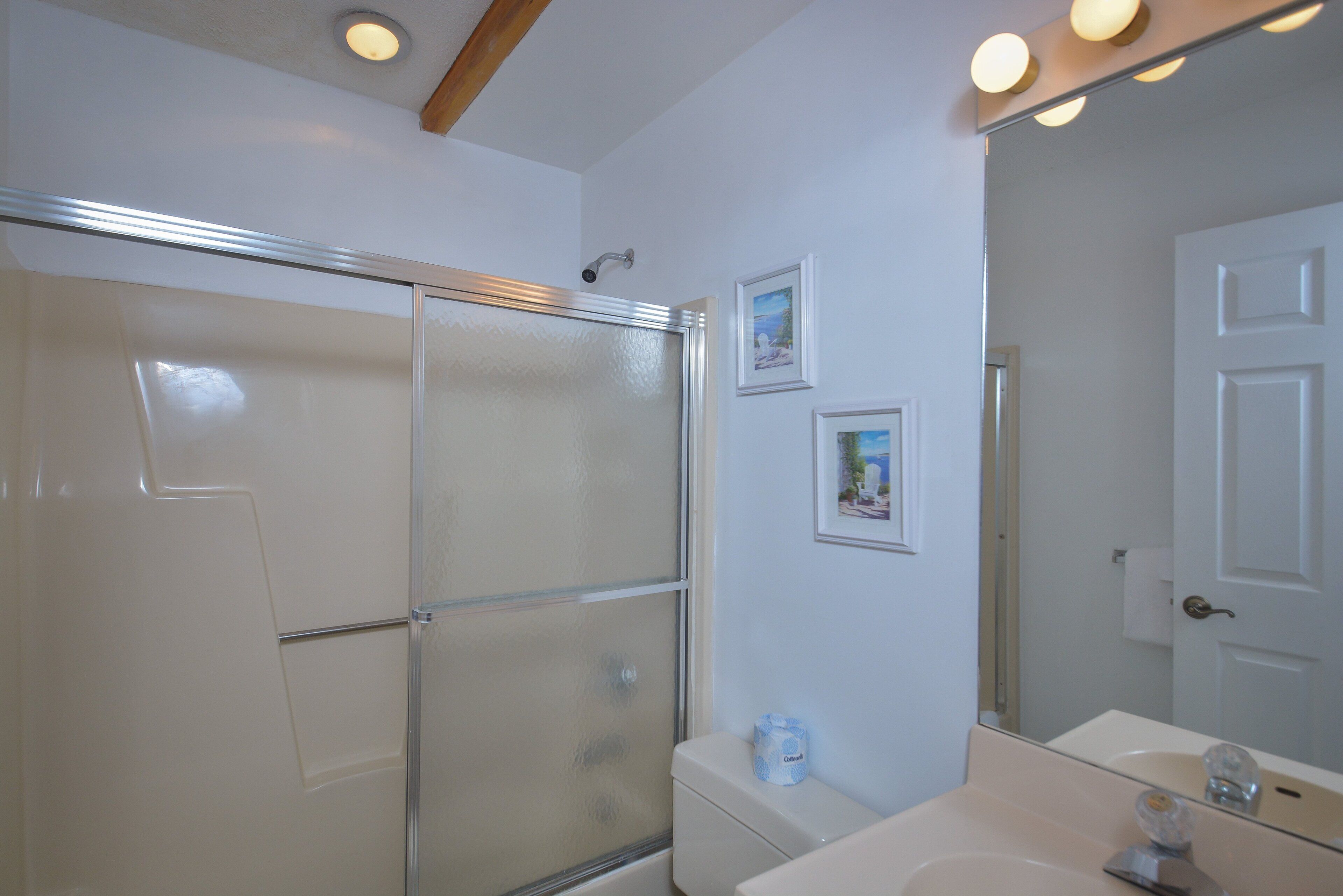 Un baño con cabina de ducha de vidrio, un lavabo blanco y un espejo con luces superiores.