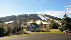 A rural landscape with a house in the foreground, a snow-covered hill in the background, and a clear sky. - Deep Creek Village #29 by Taylor Made Deep Creek (McHenry)