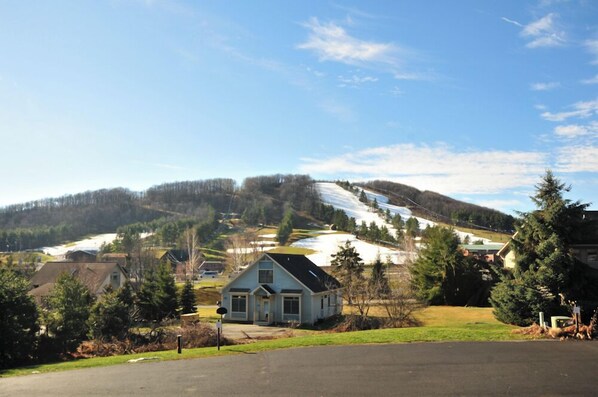 A rural landscape with a house in the foreground, a snow-covered hill in the background, and a clear sky. - Deep Creek Village #29 by Taylor Made Deep Creek (McHenry)