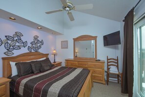 Quarto com cama, cômoda, cadeira, espelho, ventilador de teto e televisão.
