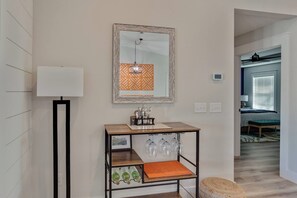 A modern living room with a wooden coffee table, a floor lamp, a wall-mounted mirror, and a decorative orange and white pattern.
