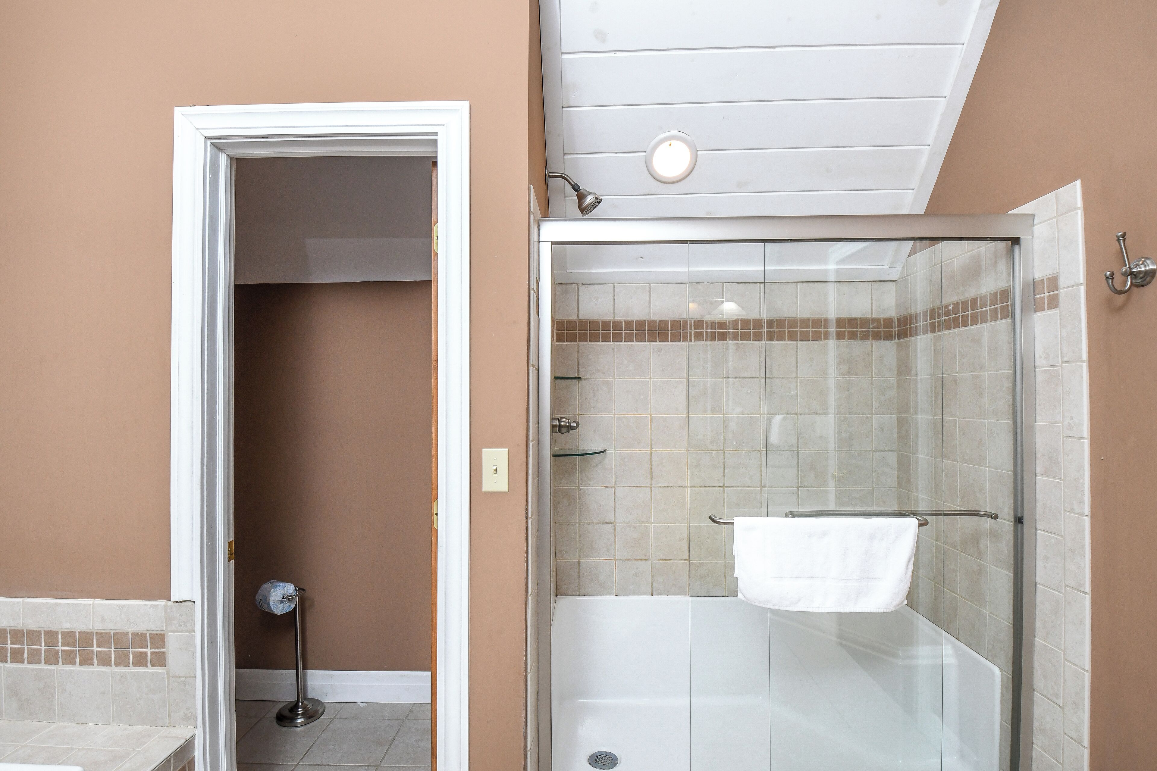 A bathroom with a glass-enclosed shower, a white bathtub, and a towel rack.