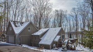 A two-story house with a sloped roof, a garage, and a deck with a railing. - Donnas Choice by Taylor Made Deep Creek (McHenry)
