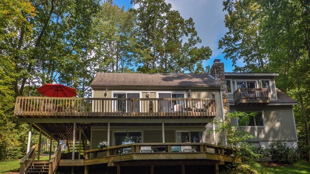 A two-story house with a deck, a covered patio, and a stone chimney. - Donnas Choice by Taylor Made Deep Creek (McHenry)