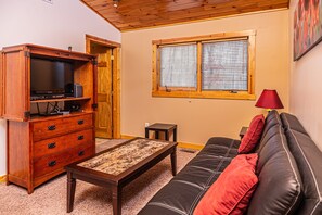 A living room with a wooden cabinet, a television, a coffee table, a sofa with red cushions, and a window with blinds. - Donovan's Dacha by Taylor Made Deep Creek (McHenry)