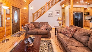 Ein gemütliches Wohnzimmer mit einer Holztreppe, Ledersofas, einem Couchtisch und einer Küchenzeile.
