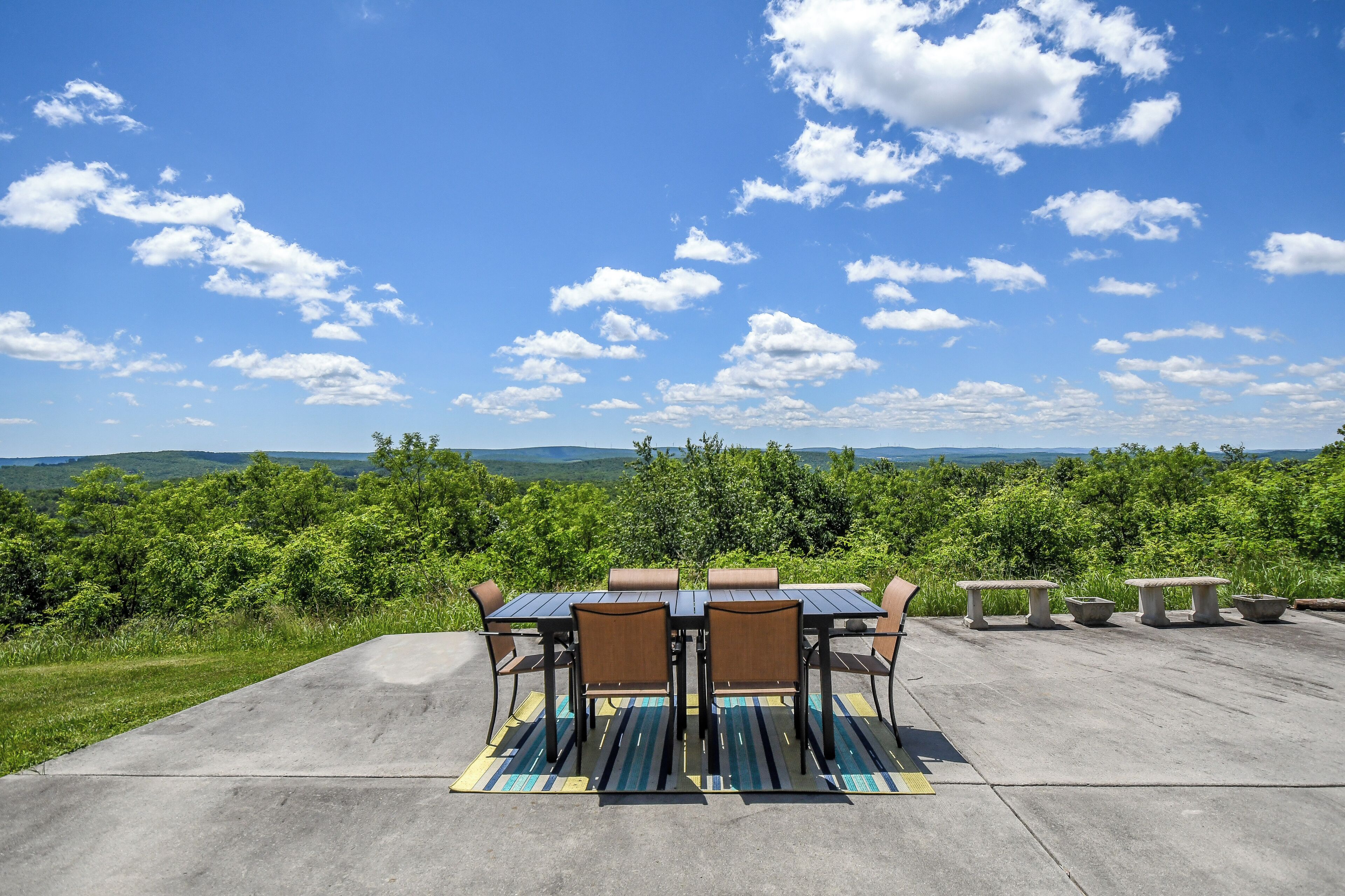 An outdoor patio with a table and chairs, surrounded by greenery and a scenic view.