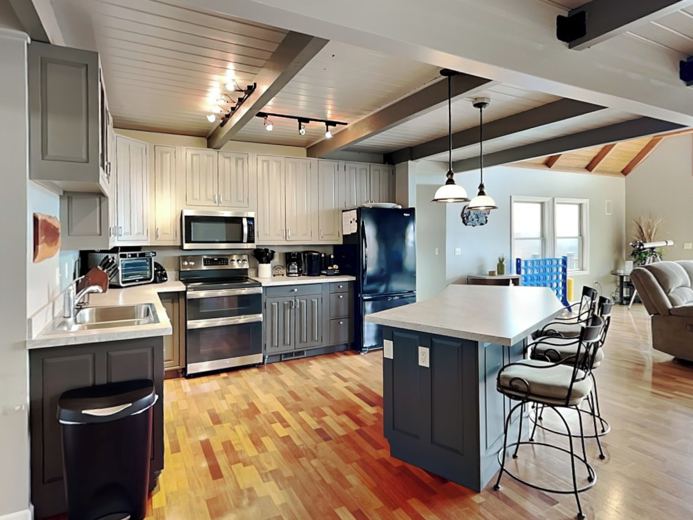 A modern kitchen with a central island, stainless steel appliances, and a herringbone wood floor.