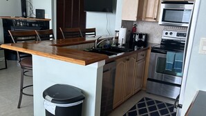 A modern kitchen with a central island, wooden cabinets, a stainless steel oven, and a dining area with chairs. - Paradise in Pensacola Beach/Gulf of Mexico (Pensacola Beach)