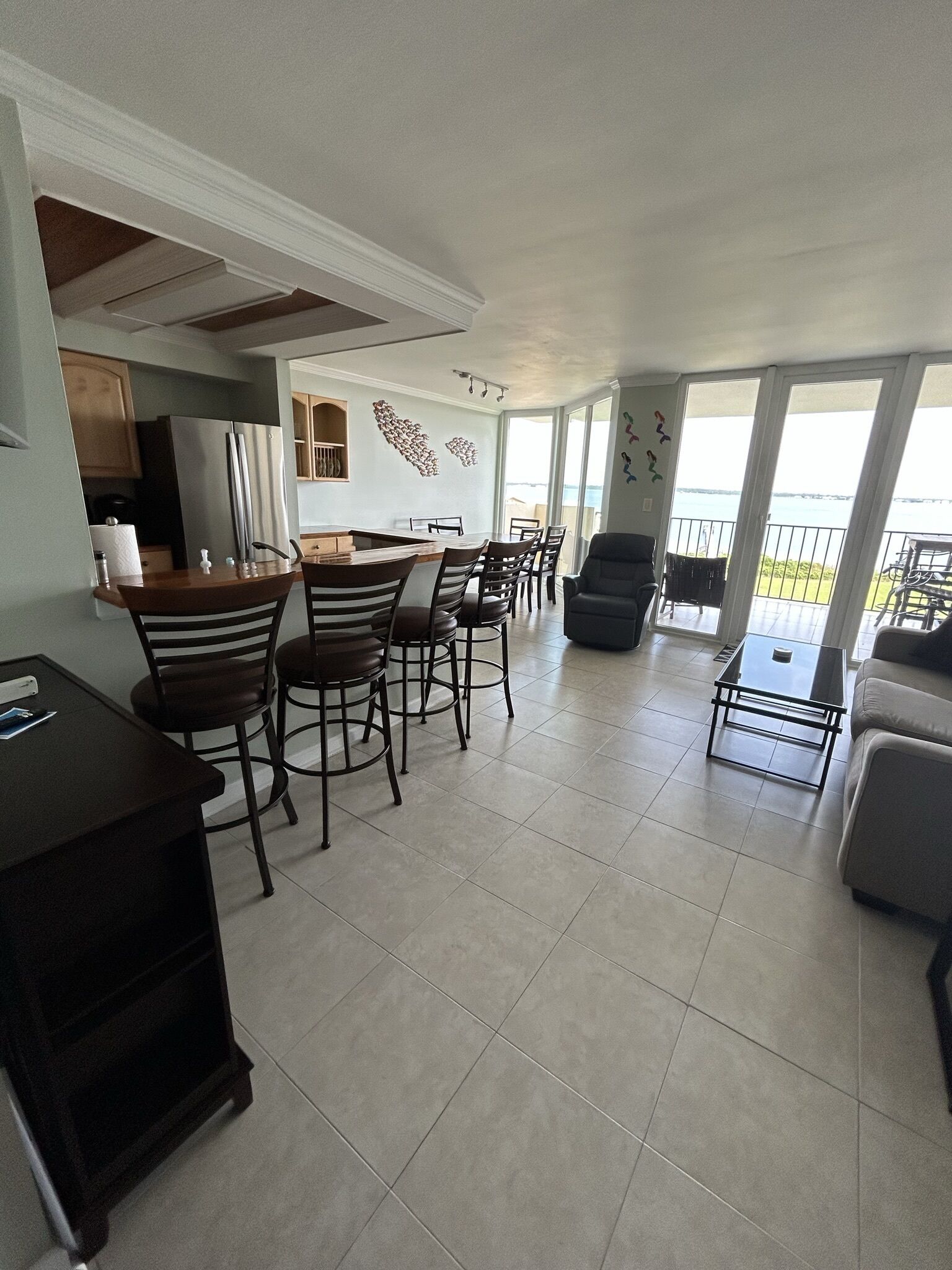 A spacious living area with a dining table and chairs, a sofa, and a balcony with a view of the sea.