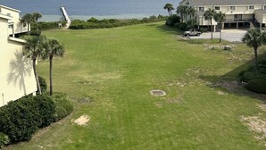 A grassy area with a dock extending into a body of water, surrounded by buildings with a number '5' on one. - Paradise in Pensacola Beach/Gulf of Mexico (Pensacola Beach)