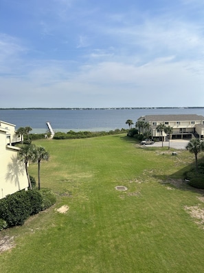 A grassy area with a dock extending into a body of water, surrounded by buildings with a number '5' on one. - Paradise in Pensacola Beach/Gulf of Mexico (Pensacola Beach)