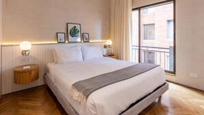 Ett modernt hotellrum med en stor säng, två sängbord med lampor, ett fönster med gardiner och inramade konstverk på väggen.