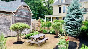 A backyard with a wooden picnic table, a small tree, and a flower bed.