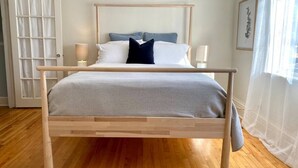 A wooden bed with a grey mattress and pillows, a bedside table with a lamp, and a door with frosted glass panels.