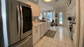 A modern kitchen with stainless steel appliances, white cabinets, and a tiled floor. - 5 Miles to the beach, family home, saltwater pool, pickleball & tennis courts (Naples)
