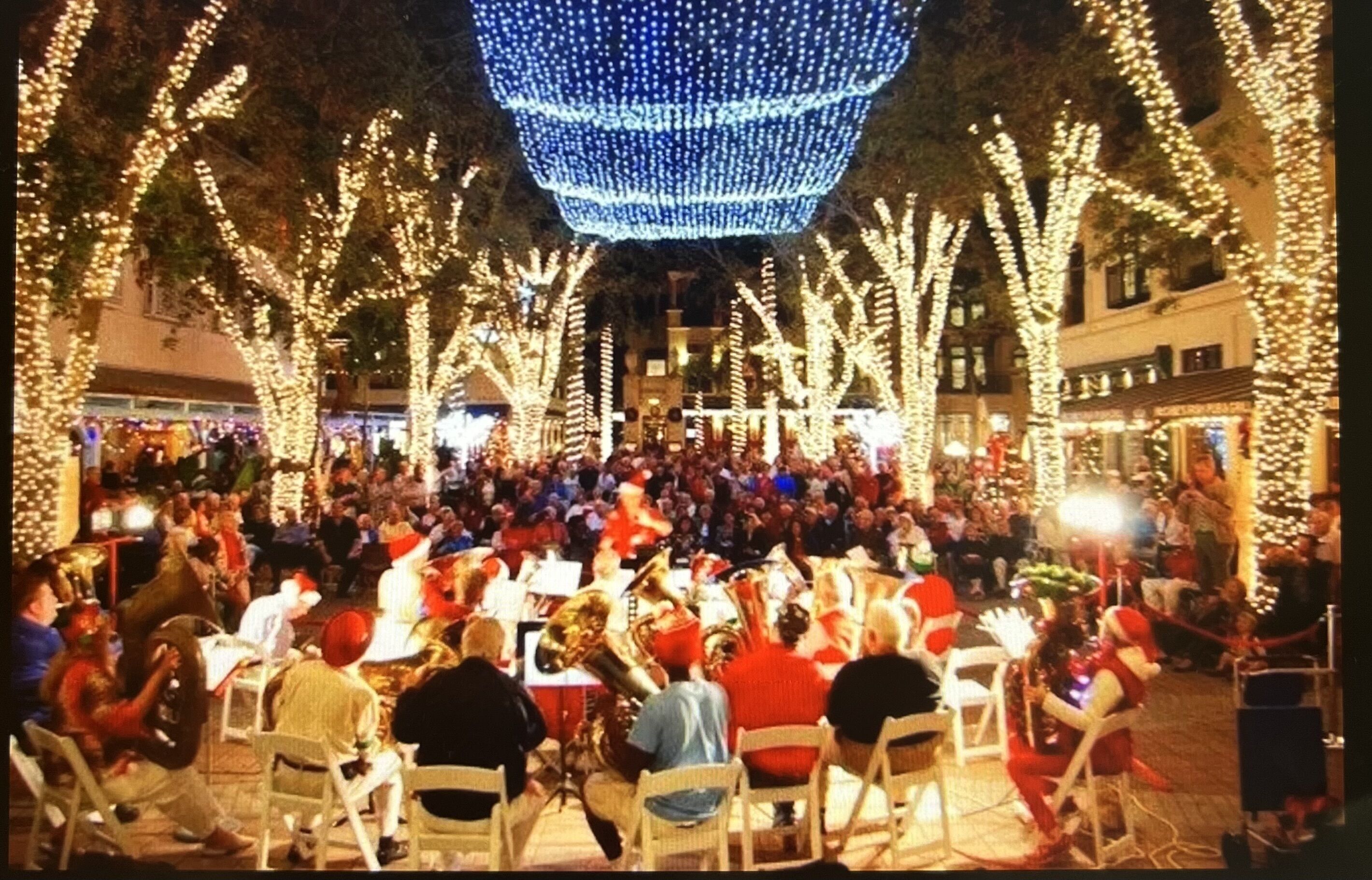 Un espacio al aire libre con mesas y sillas, rodeado de árboles decorados con luces.