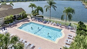A swimming pool with lounge chairs and palm trees, overlooking a body of water and buildings. - 5 Miles to the beach, family home, saltwater pool, pickleball & tennis courts (Naples)