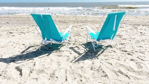 Dos sillas de playa turquesa sobre arena, con el océano al fondo.
