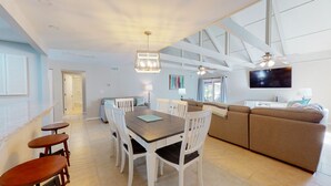 A spacious living area with a dining table, white chairs, a sofa, and a television mounted on the wall. - Two Bedroom Villa Steps from Robert Trent Jones Golf Course! (Hilton Head Island)