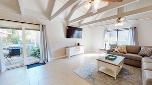 A spacious living room with a flat-screen TV mounted on the wall, a sofa, a coffee table, and a sliding glass door leading to an outdoor area. - Two Bedroom Villa Steps from Robert Trent Jones Golf Course! (Hilton Head Island)