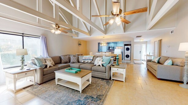 A spacious living room with a large sectional sofa, a coffee table, and a ceiling fan. There is a kitchen area visible in the background. - Two Bedroom Villa Steps from Robert Trent Jones Golf Course! (Hilton Head Island)