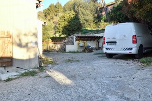 Un camino de grava que conduce a una furgoneta blanca estacionada cerca de un edificio con un muro de piedra y una puerta de madera.