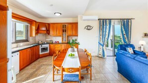 A modern kitchen with wooden cabinets, a dining table with chairs, a built-in oven, and a potted plant. - Villa Wisteria - Three Bedroom Villa, Sleeps 6 (Latchi)