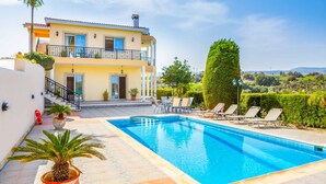 A two-story building with a swimming pool, outdoor seating, and a view of the countryside. - Villa Wisteria - Three Bedroom Villa, Sleeps 6 (Latchi)