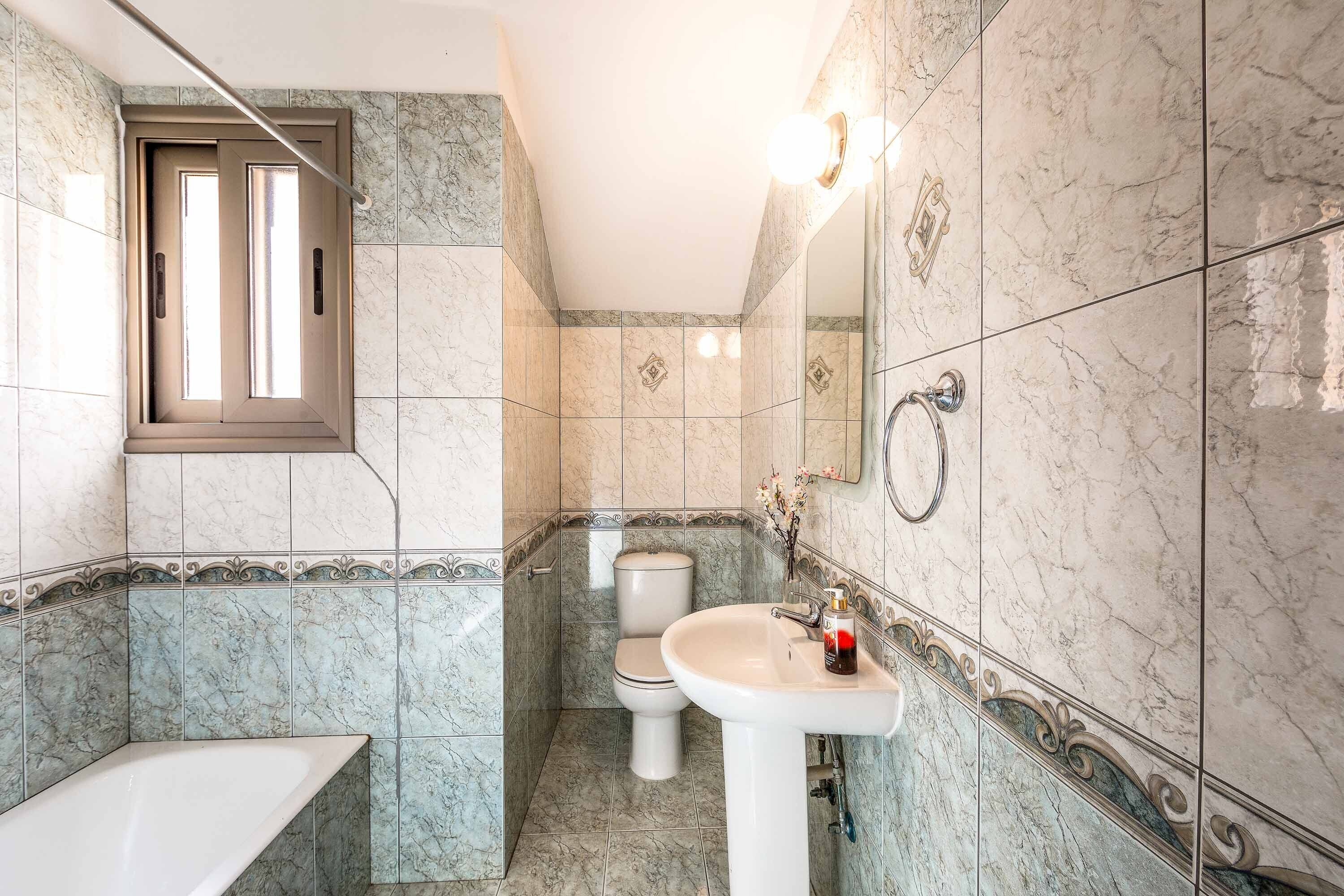 A bathroom with a toilet, sink, and bathtub, featuring marble tiles and a window.
