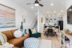 Ein modernes Wohnzimmer mit einer braunen Couch, einem grünen Sessel und einem Essbereich mit einem Holztisch und Stühlen. Eine Treppe führt zu einer oberen Ebene.