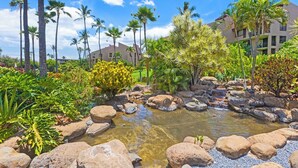 A landscaped garden with a pond, palm trees, and a building in the background. - here Elegance Meets the Breeze Kihei Renovated 2BR Condo Full Ocean Views (Kihei)
