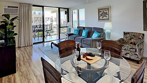 A spacious living room with a glass-top dining table, a sofa, and a chair. - here Elegance Meets the Breeze Kihei Renovated 2BR Condo Full Ocean Views (Kihei)