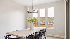 Uma sala de jantar com uma mesa de madeira, cadeiras pretas, um vaso com flores e um candelabro.