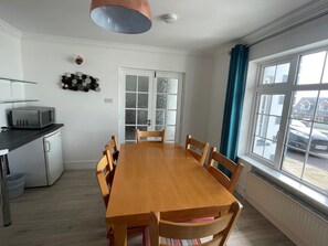 A dining area with a wooden table and chairs, a microwave on a counter, and a window with curtains.