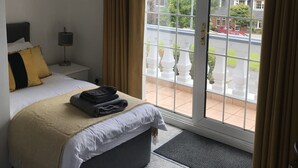 Ein Schlafzimmer mit Bett, Nachttisch, Lampe, einem Fenster mit Vorhängen und Blick nach draußen.