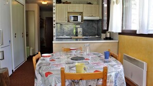 A compact kitchen with a microwave, sink, and cabinets. A dining table with chairs is set up in the center. - 250m from resort center, 3rd floor, terrace, tv, ski locker, 45m², Risoul (Risoul)