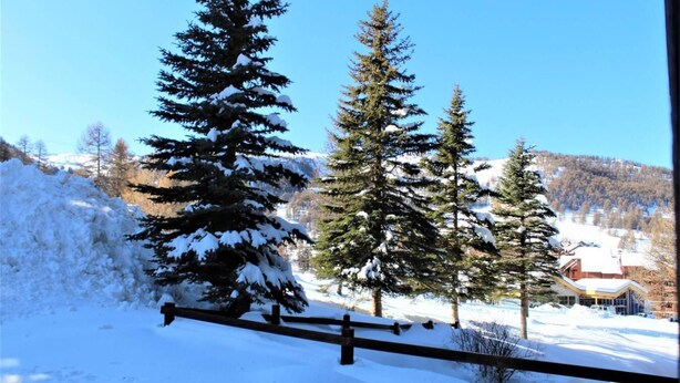 A snowy landscape with a wooden fence, evergreen trees, and a building in the background. - 250m from resort center, 3rd floor, terrace, tv, ski locker, 45m², Risoul (Risoul)