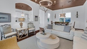 A spacious living room with a high ceiling, a dining area with a wooden table and chairs, and a cozy seating area with a sofa and armchairs.