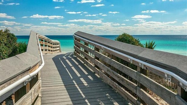A wooden boardwalk leading to a beach with a clear view of the ocean and a blue sky.