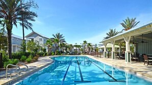 A swimming pool with clear blue water, surrounded by palm trees and a covered patio area with outdoor seating.