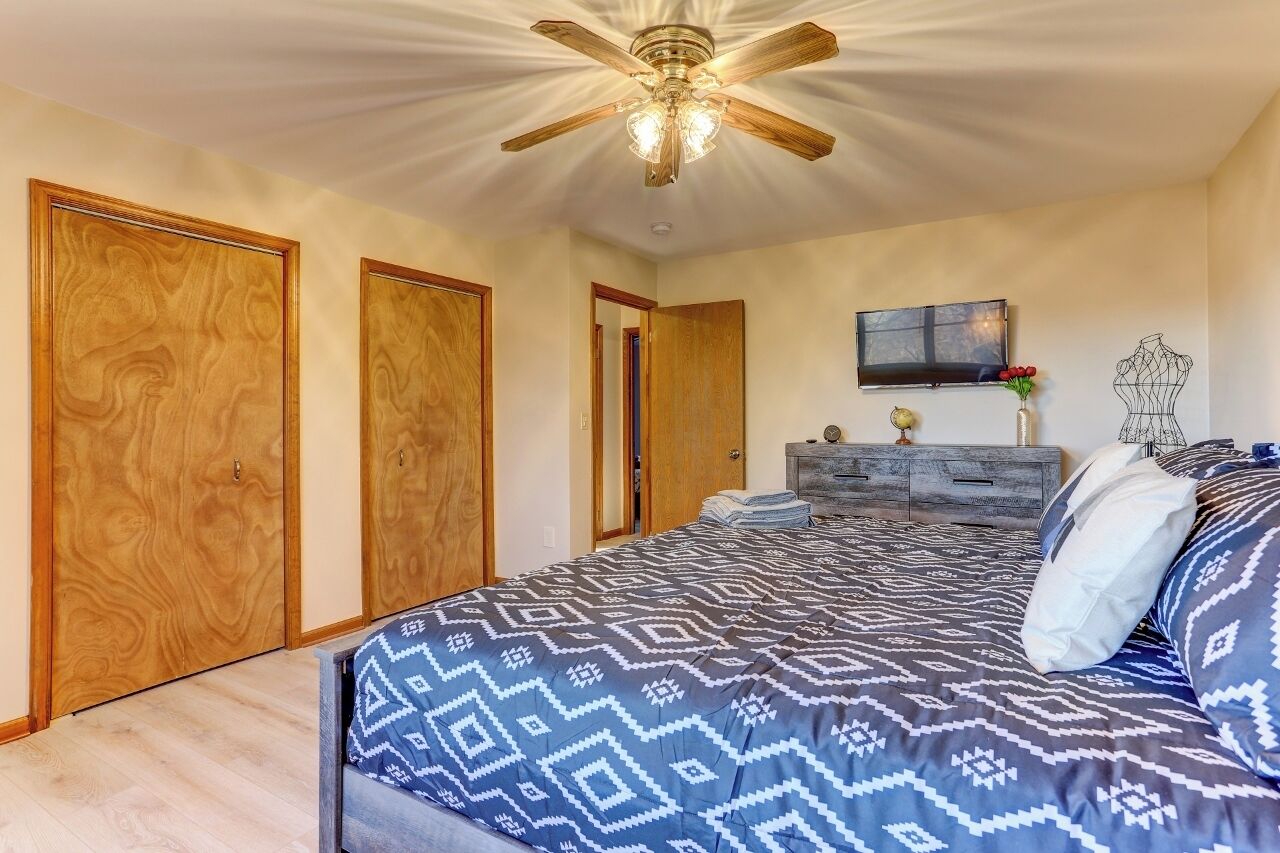 A bedroom with a bed, wooden wardrobes, a ceiling fan, a TV, and a dresser.