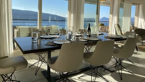 En matplats med ett bord för fyra personer, stora fönster med utsikt över havet och bergen samt modern takbelysning.
