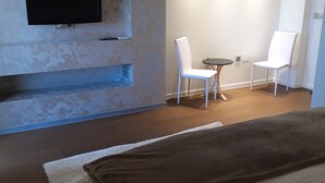 Une chambre d’hôtel moderne dotée d’un grand lit, d’un téléviseur à écran plat fixé au mur, d’une petite table ronde avec deux chaises blanches et d’un éclairage encastré au plafond.