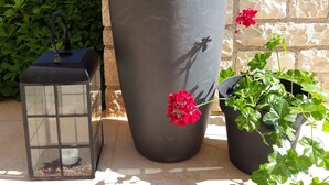 Un grand bac à fleurs orné d’une sculpture d’oiseau, d’une lanterne et d’une plante en pot aux fleurs rouges.