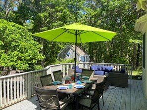 Une terrasse avec une table dressée pour le repas, entourée de meubles en osier et agrémentée d’un parasol vert vif.