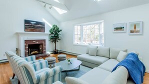 A living room with a fireplace, striped chairs, a sofa, and a large window. - Modern Family Getaway In Harwich (Harwich)