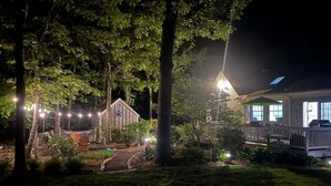 A residential property at night with a well-lit garden, a wooden fence, and a house with a porch. - Modern Family Getaway In Harwich (Harwich)