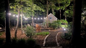 A garden with a wooden structure, string lights, and a paved path. - Modern Family Getaway In Harwich (Harwich)