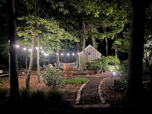 Un jardin agrémenté d’une structure en bois, de guirlandes lumineuses et d’un chemin pavé.